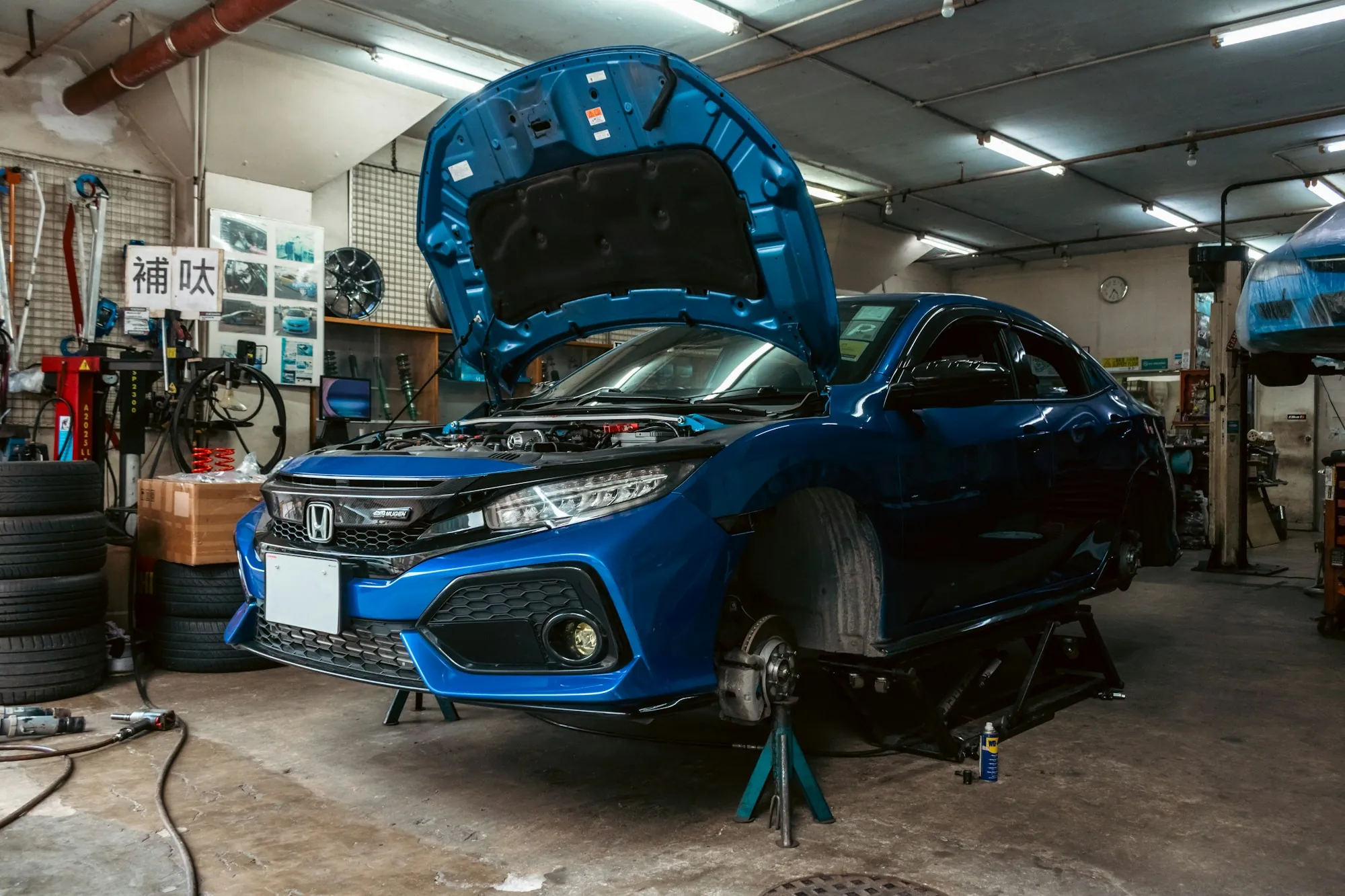 Blue car raised on a lift inside a well-equipped repair shop