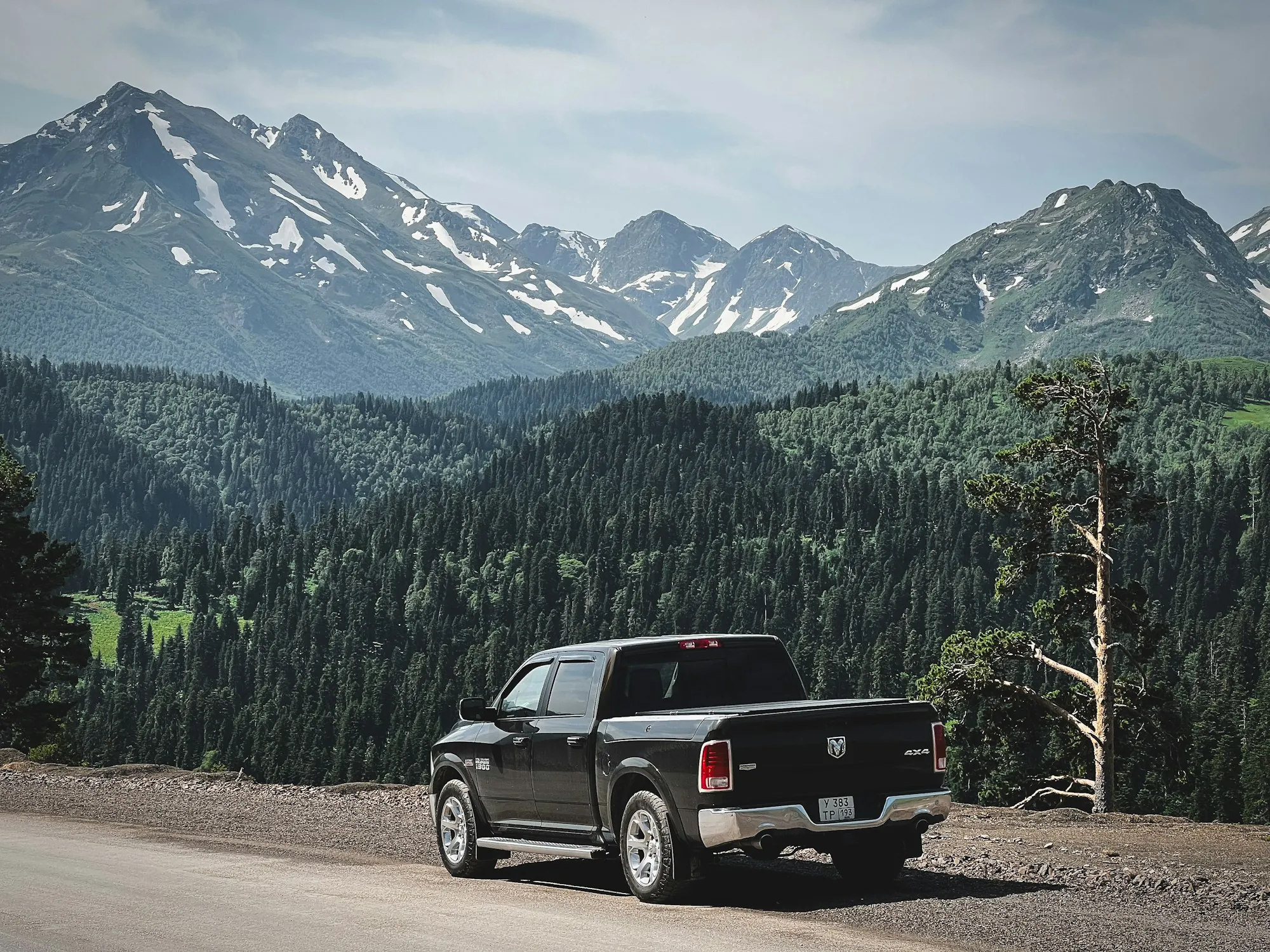 Pickup truck below snow-capped peaks and forested hills